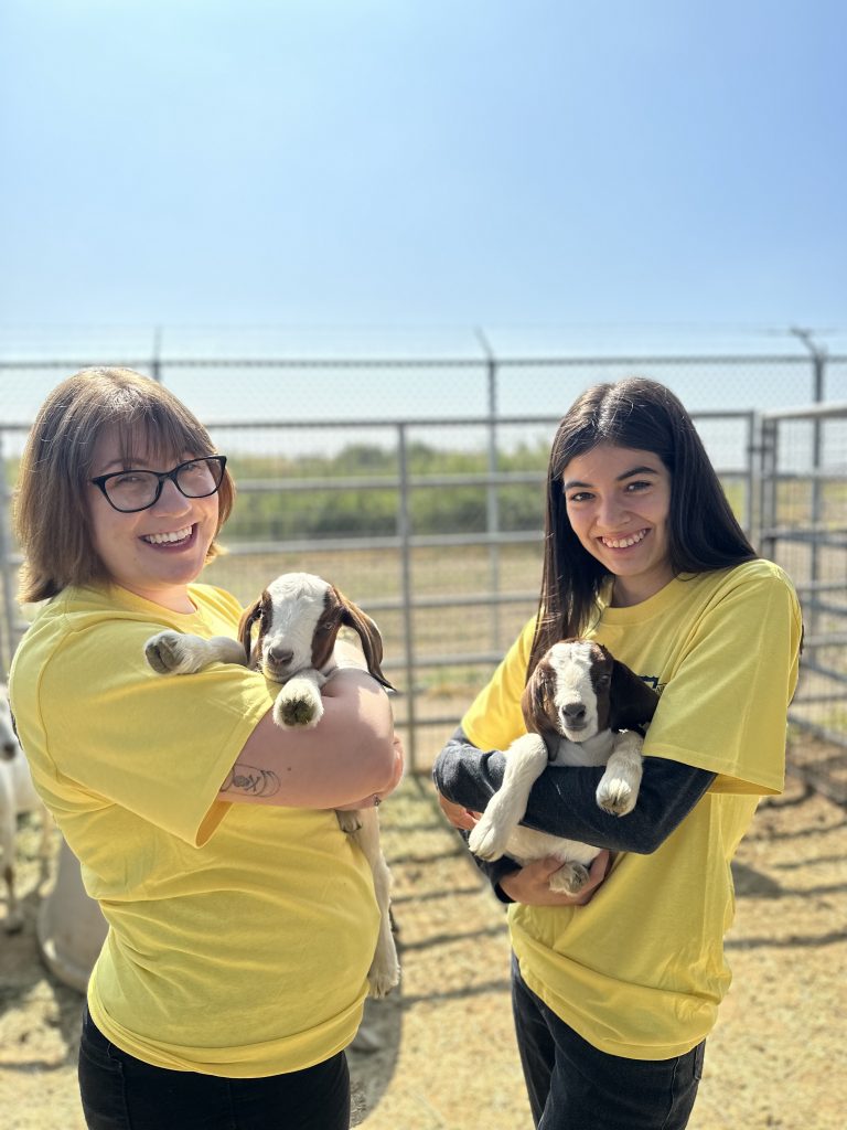 Two Animal Care volunteers are seen holding a baby goat in each of their arms