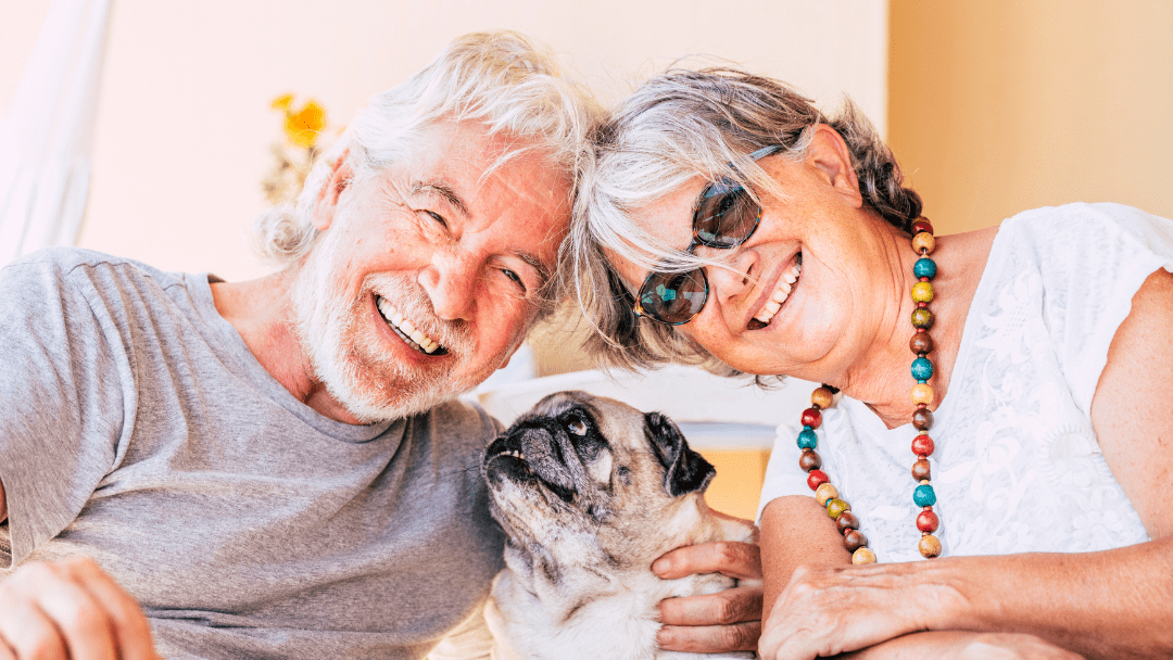 An older couple smiling together with their aging pug.