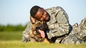 A military personnel member hugging a German Shepherd outdoors
