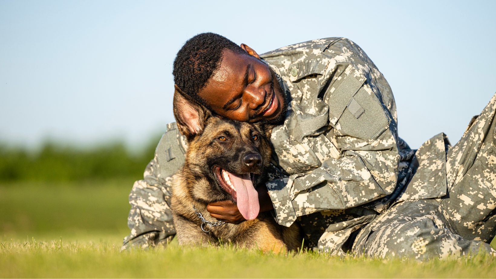 A military personnel member hugging a German Shepherd outdoors